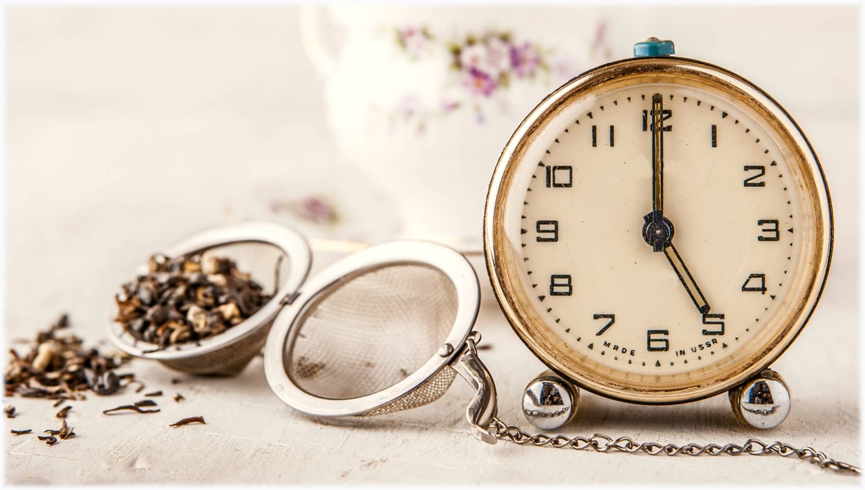 Vintage alarm clock with tea strainer on the white table