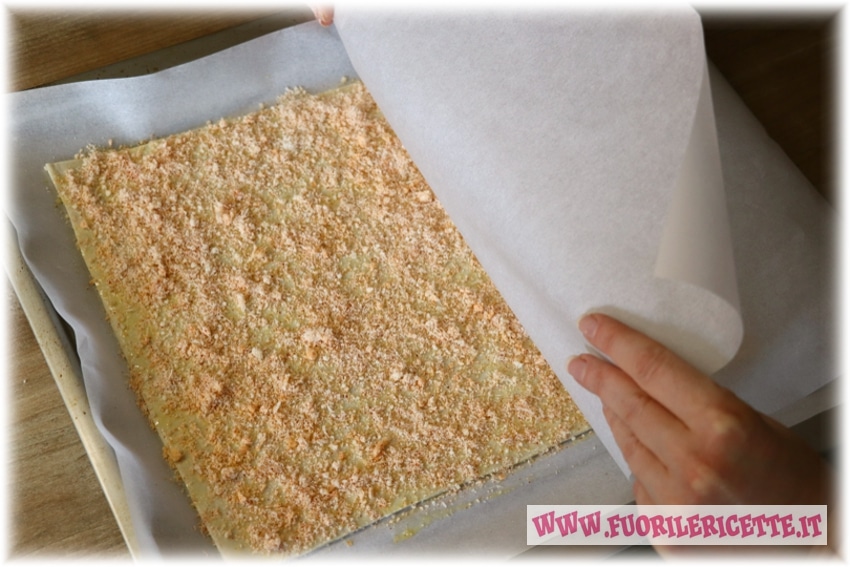 Adagiamo la carta forno sopra la sfoglia e premiamo leggermente per far attaccare il formaggio alla pasta.